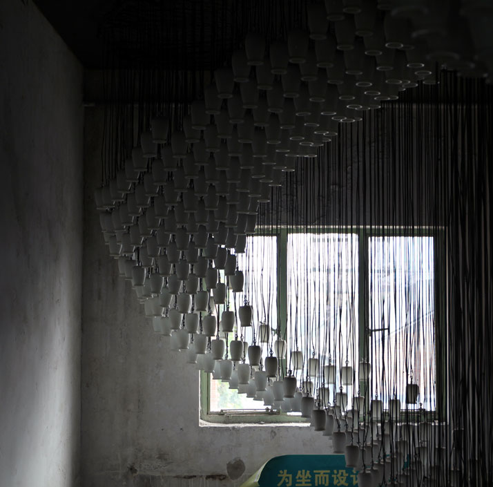 Milkywave by AIDIA STUDIO. It consists of 1664 reused glazed ceramic yoghurt bottles reconstituted into a looping wave of light.  Although this instal