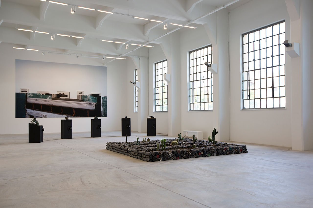 Installation View Portals, Hellenic Parliament + NEON at the former Public Tobacco Factory, Photography © Natalia Tsoukala. Courtesy NEON
Featured:
Jannis Kounellis, Untitled, 2005. Lead, clothes, earth, cacti. 85 × 360 × 360 cm. Private Collection Rome, Italy.
Liliane Lijn, Early Events, 1996-2000. Five sculptures, patinated bronze, freestanding painted MDF bases and media players. Dimensions variable Courtesy the artist and Rodeo, London / Piraeus.
Louise Lawler, Cities (adjusted to fit), 2004/2005/2015. Adhesive wall material. Dimensions variable to match proportions of a given wall at any scale determined by exhibitor. Courtesy the artist, Metro Pictures, New York, Sprüth Magers.