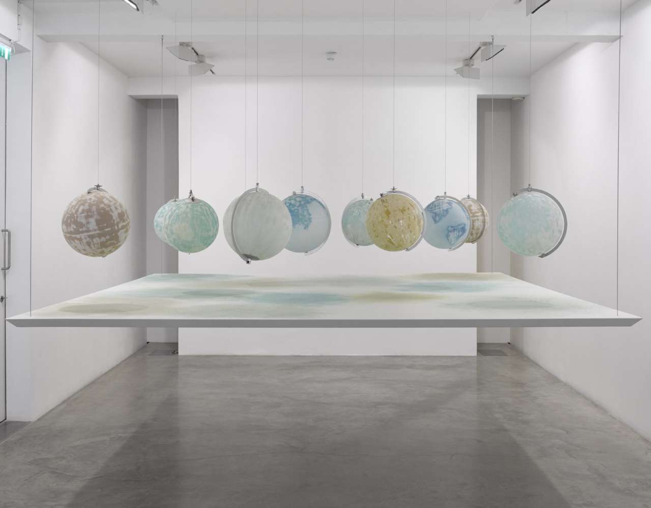 Julian Charrière, We Are All Astronauts, 2013. 11 found globes made of glass, plastic and paper, abraded with international mineral sandpaper, suspended table top, dust from globes’surfaces. Courtesy the artist; DITTRICH &amp; SCHLECHTRIEM, Berlin; Galerie Tschudi, Zuoz; Sean Kelly, New York; Sies+Höke, Düsseldorf.